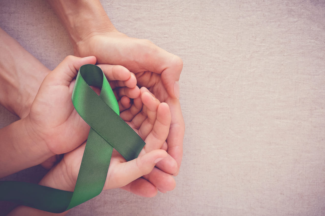 Green Ribbon for Liver Cancer Awareness being supported by adult and child hands. Donate today